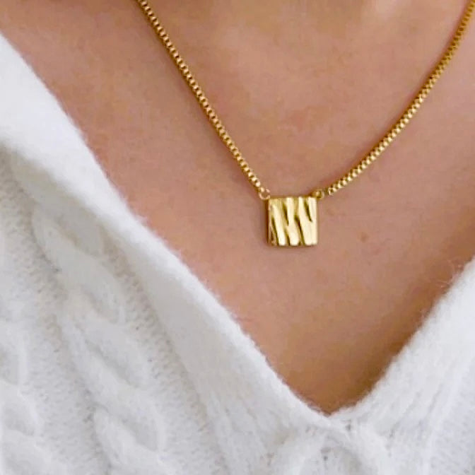 Woman accessorizing her white sweater with a the gorgeous gold plated square textured pendant. 