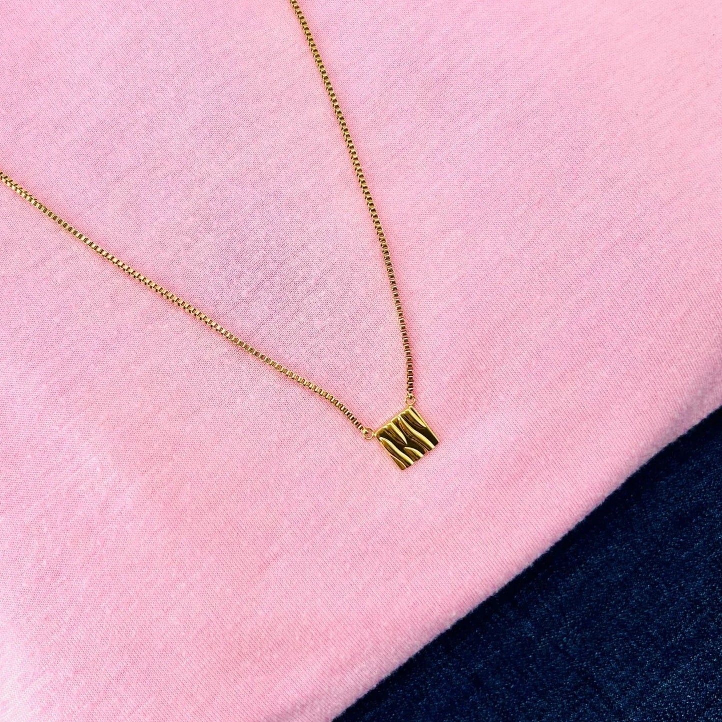 The gold square pendant on a pale pink shirt and jean, showing it's versatility with every outfit.rsatilityh 